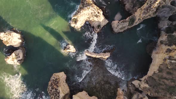 Seagulls flying over rocks and cliffs. Waves washing up. Ascending top down aerial, Lagos, Algarve