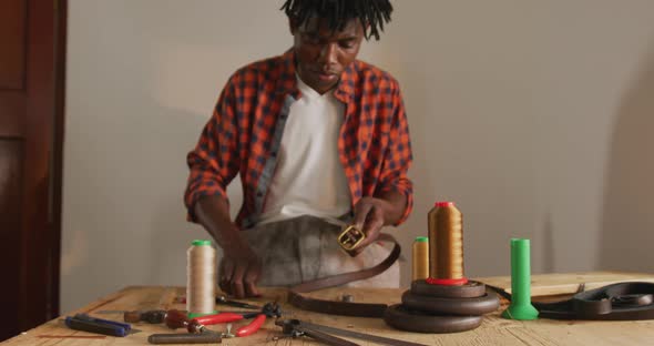 Focused african american craftsman using tools to make a belt in leather workshop