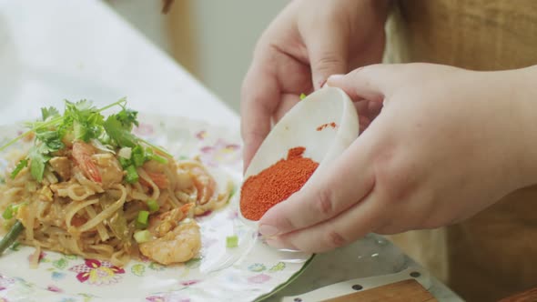 Woman adding ground red pepper to wok noodles