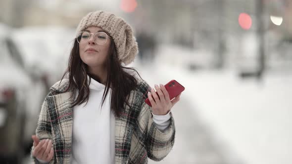 Portrait of a Beautiful Young Darkhaired Woman in Round Glasses and a Plaid Coat Walking on a Snowy