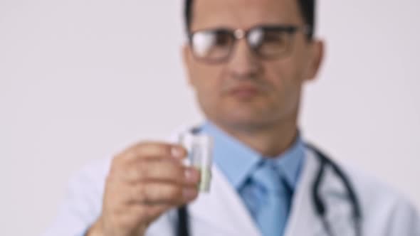 Serious Doctor Holds Transparent Jar with Green Pills and Spills Them Down