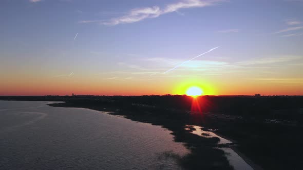An aerial view over a bay during sunset with a drone camera. The sun is on the horizon & it is about