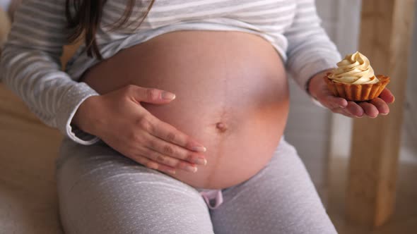 Closeup of a Pregnant Woman Holding a Sweet Cake While Sitting on the Bed