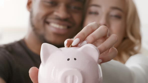 Family Savings Happy Multiracial Couple Putting Coin In Piggybank Indoors