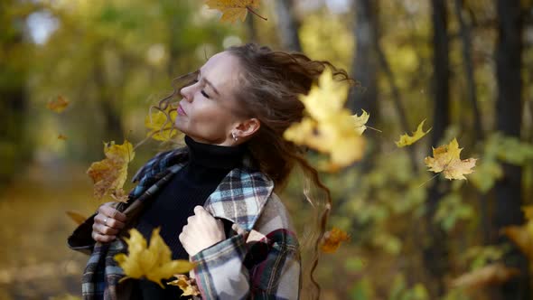 a Blonde with Long Hair and a Plaid Coat Walks Through the Autumn Park Through Falling Leaves and