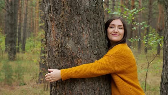 Happy Woman Hiker Embraces Old Pine Tree Trunk in Forest