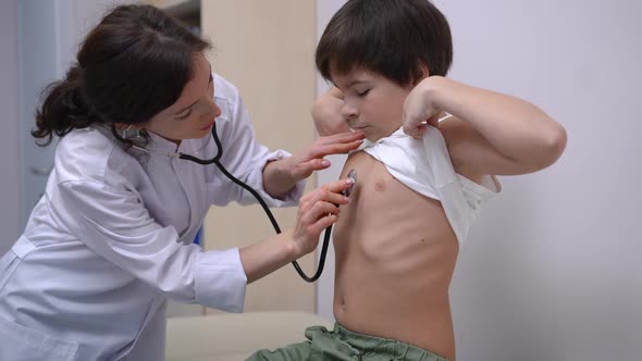 Caucasian Ill Boy Raising Tshirt As Doctor Listening Auscultation in Hospital