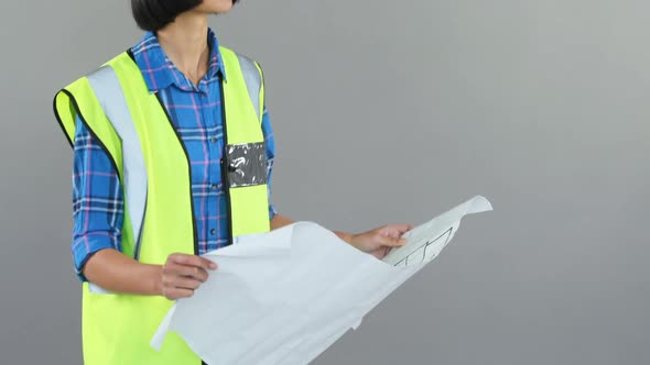 Female architect looking at blueprint against grey background 4K 