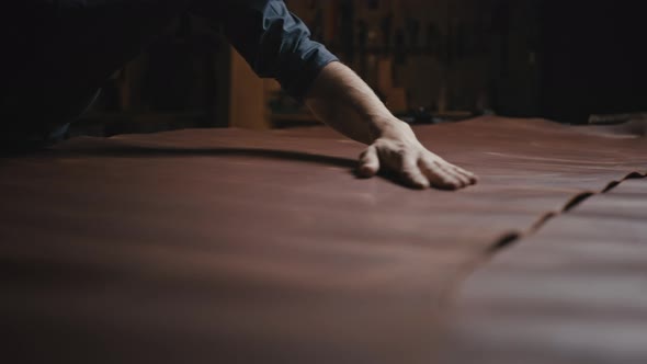 Unrecognizable Man Tailor Smoothing Out Leather on Table Examining Fabric Quality Before Work with