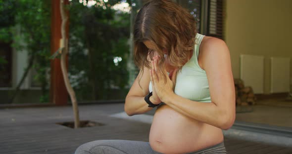 Relaxed caucasian pregnant woman practicing yoga in patio