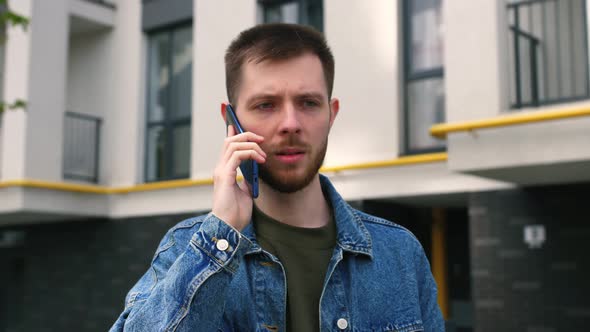 Stressed Young Man Hearing Awful News at Mobile Phone Call Conversation Outside