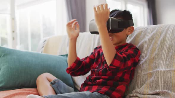 Happy asian boy at home, sitting on couch in living room wearing vr headset