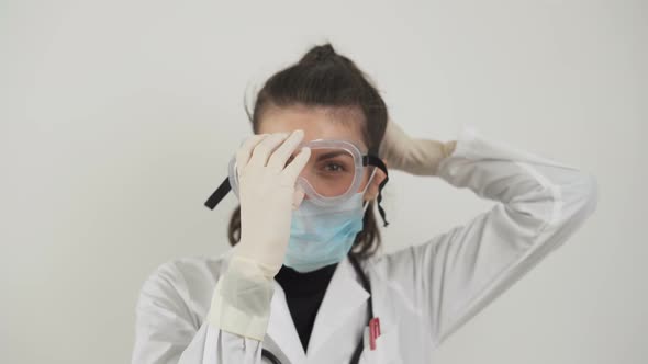Young Female Doctor Puts Protective Plastic Glasses and Facemask Against Coronavirus