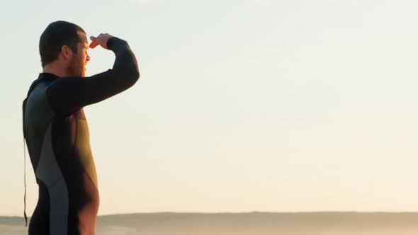 Side view of mid-adult caucasian male surfer with shielding eyes looking at sea at beach 4k