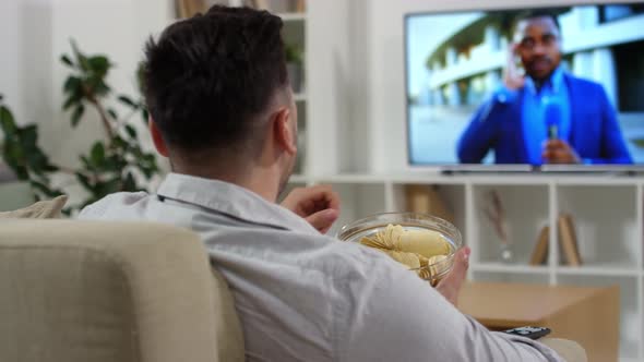 Man Eating Chips and Watching News on TV