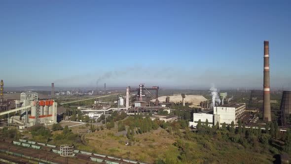 Blue sky with white clouds against the background of a metallorgic plant smoking with black smoke.