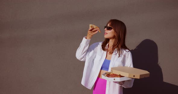 girl takes a triangle of pizza from the box, raises it above herself and eats it
