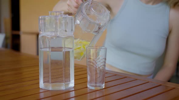 A Woman Pours a Tonic Drink with Lemon and Honey From a Decanter Into a Glass