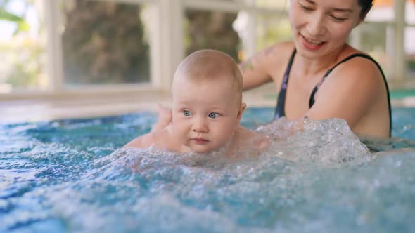 Happy Mother in Red Swimming Suit with Baby Son Surfing Water with Fun in Swimming Pool