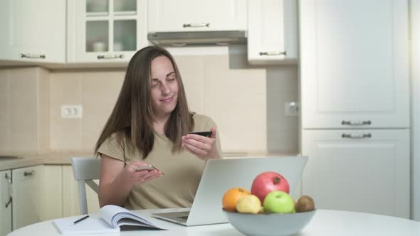 Young woman shopping online with credit card and laptop  at home on the kitchen.