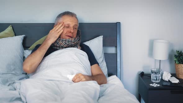 A Sick Middleaged Man is Lying in Bed and is Suffering at Home From a Headache and a Severe Cold