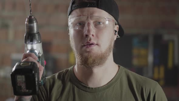 Portrait of Confident Bearded Worker Raises the Drill Screwdriver and Presses the Button 