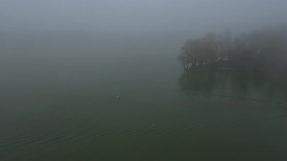 Alone Man is Floating on a Board on a River in a Very Thick Fog