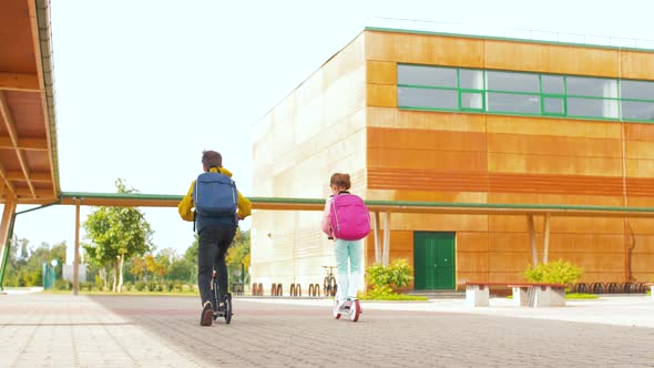 School Children with Backpacks Riding Scooters