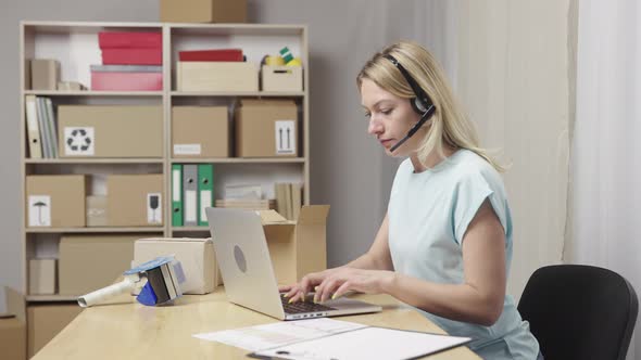 Female Postal Worker with Headset Working on Laptop at Post Office and Typing on Keyboard