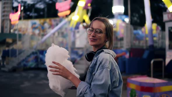 Traking Footage of a Young Blonde Girl Walking in the Amusment Park Eating White Candy Cotton