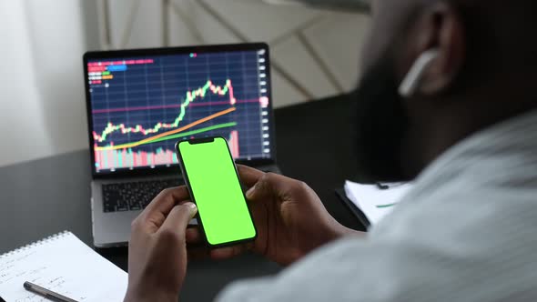 African American Cryptocurrency Trader Investor Holds in Hand Cell Phone with Green Mockup Screen