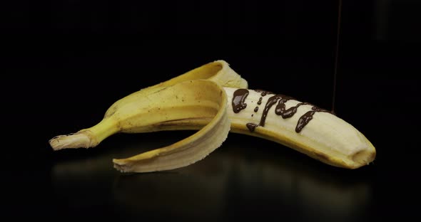 Pouring a Banana with Melted Dark Chocolate Syrup Black Background