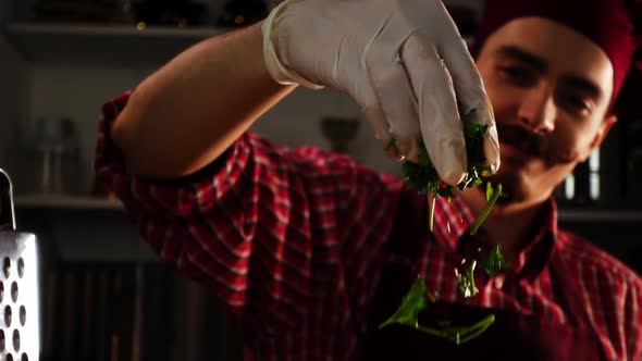 Smiling Cook in a Red Toque is Sprinkling Fresh Parsley While He is Preparing Dinner in Slow Motion