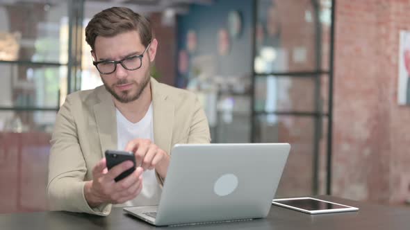 Young Man with Laptop Using Smartphone