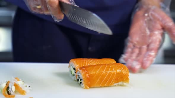 Chef cuts sushi with sharp knife into pieces. 