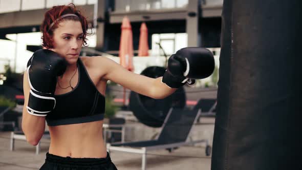 Beautiful Female Boxer Punching a Bag Outside