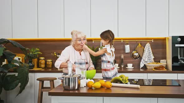 Grandmother is Whipping Eggs and Her Little Grandchild is Staining Grannys Nose in Flour They Going