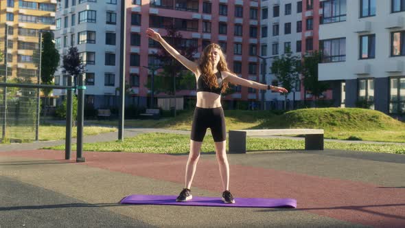 Young Woman in Black Sportswear is Stretching on Sports Ground and Bending to Left and Right