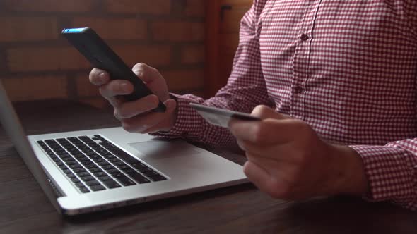 Businessman in checkered shirt making online payment with credit card and smartphone