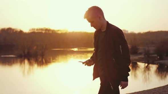 Young Man Uses Smart Phone and Walks at Beautiful Sunset on the Beach