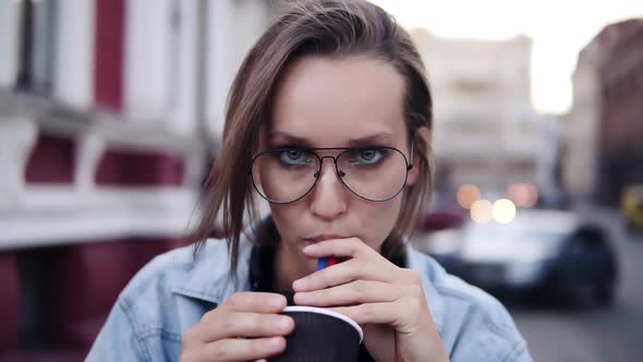 Gorgeous Blonde Girl with a Light Day Make Up Looking at the Camera Drinking Beverage with a Straw