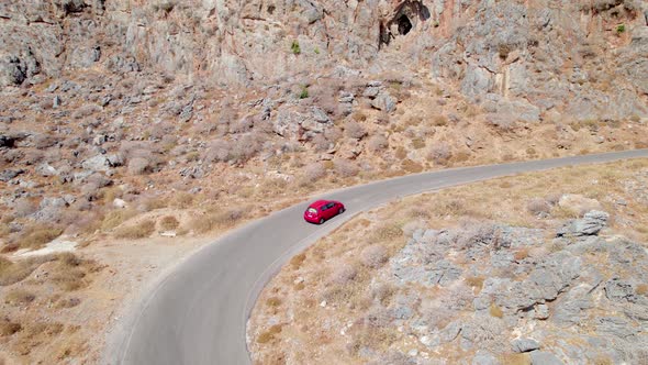 Aerial drone shot of red car driving along the narrow coastal road above rocks