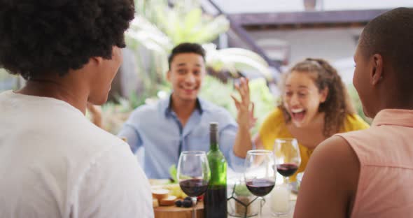 Group of diverse male and female friends drinking wine and laughing at dinner party on patio