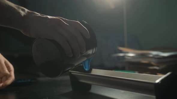 Young Caucasian Man Pouring Container with Blue Color in Workshop in Industrial Print Studio