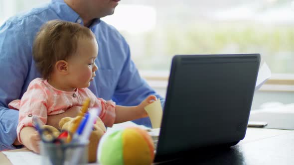 Father with Baby Working on Laptop at Home Office
