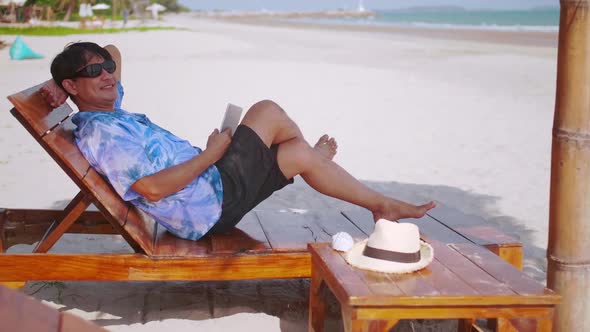 Businessman spends his weekends relaxing at the beach. Senior Asian man relaxing on the beach.