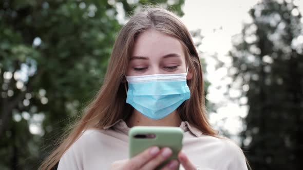 Business woman in medical face mask using smartphone typing message on mobile phone outdoor.