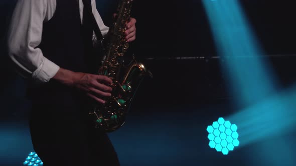 A Young Retro Stylish Guy Plays on the Golden Shiny Saxophone in the Turquoise Spotlights on Stage