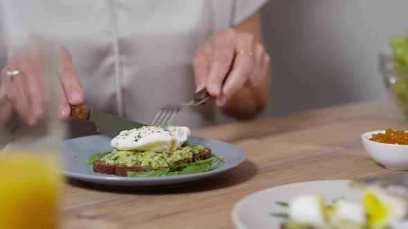 Unrecognizable Woman Cutting Poached Egg with Runny Yolk on Toast