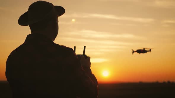 Silhouette of a Farmer Using a Drone in a Wheat Field at Sunset. Concept Technology Innovations for